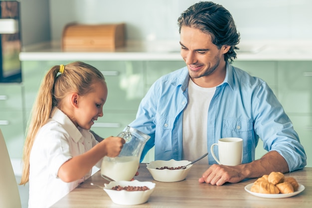 Grl and her father are having breakfast in kitchen at home.