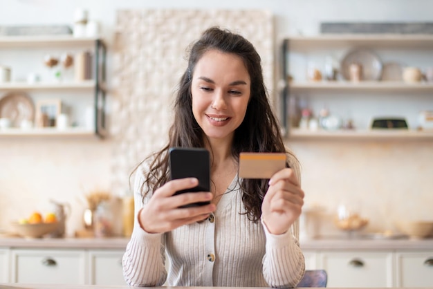 Grocery shopping app cheerful woman using credit card and cellphone buying food online while sitting