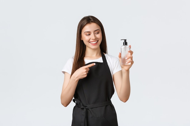 Grocery store employees, small business and coffee shops concept. Friendly-looking charismatic female barista in black apron suggest visitors use hand sanitizer for safety during pandemic.