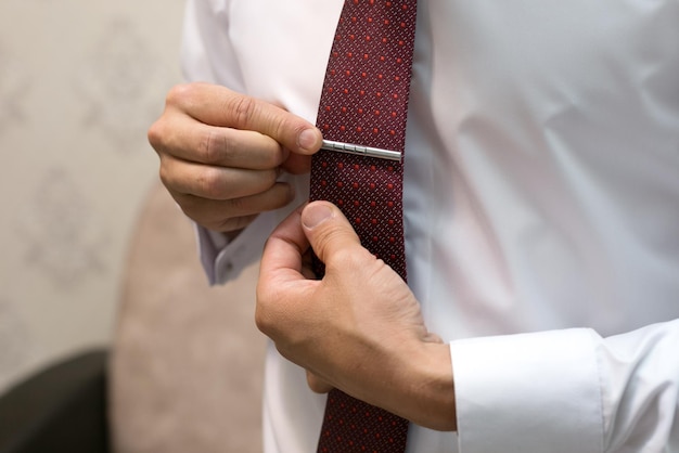 The groom adjusts the clip on the burgundy tie packing for the wedding