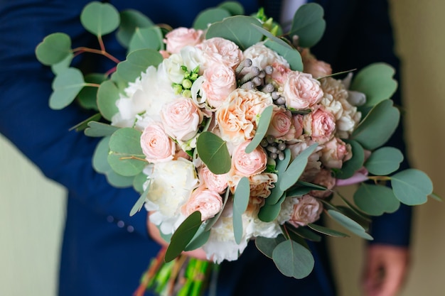 Groom in blue suit holds a beautiful wedding bouquet of roses.