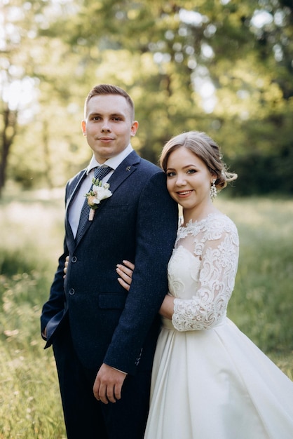 The groom and the bride are walking in the forest near a narrow river on a bright day