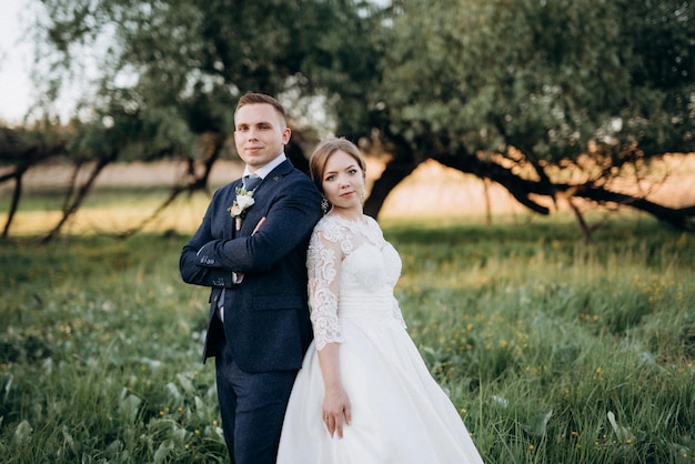 The groom and the bride are walking in the forest near a narrow river on a bright day