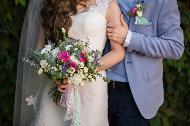 Groom embraces bride, bride holding wedding bouquet.