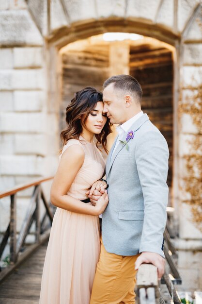 Groom gently hugs bride in a beautiful dress while standing on the bridge leading to the castle