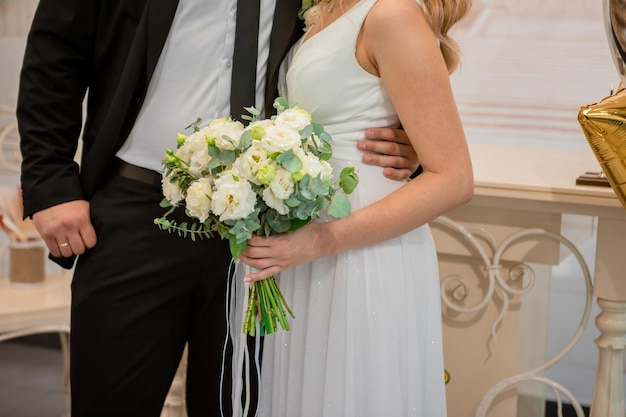 Groom holding a wedding bouquet in the hands standing near bride