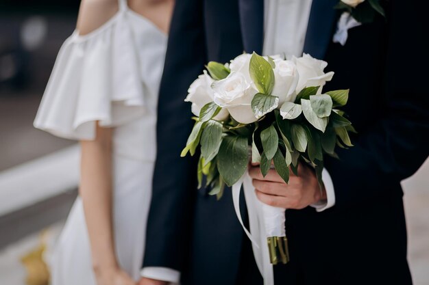 Groom holding a wedding bouquet in the hands standing near bride