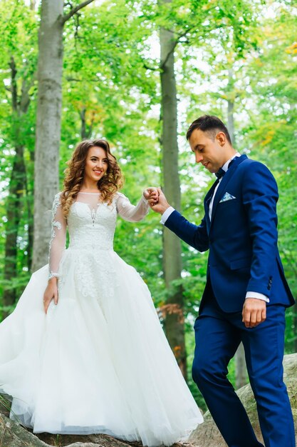 The groom holds the bride by the hand and they walk in the forest