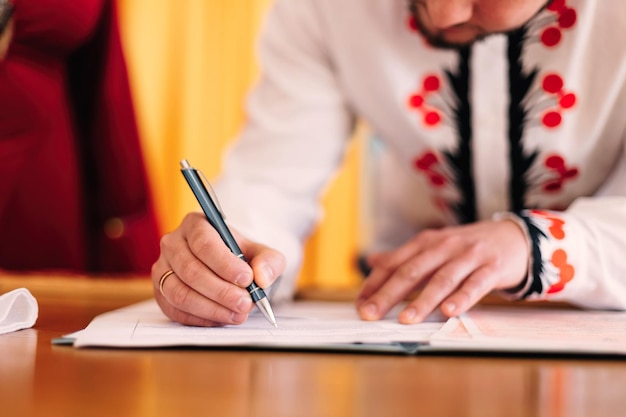 The groom holds the pen and puts a signature in the notebook ce