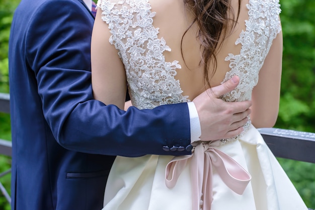 Groom hugging bride standing with his back to the camera on the bridge the day of the wedding closeup