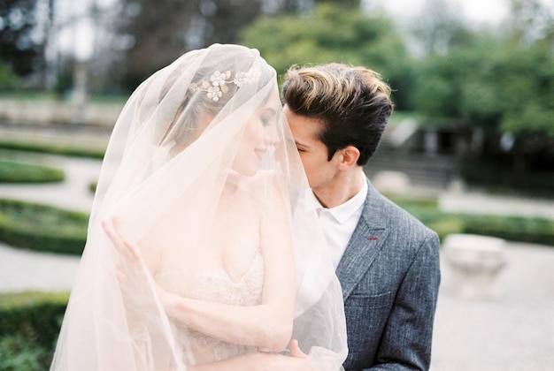 Groom hugs and almost kisses bride from behind her in the park