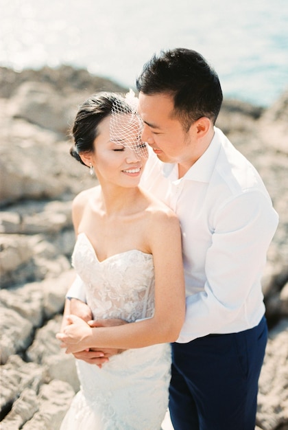 Groom hugs bride from behind and looks into her face