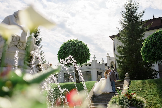 Groom hugs his bride. Shot through a fountain.