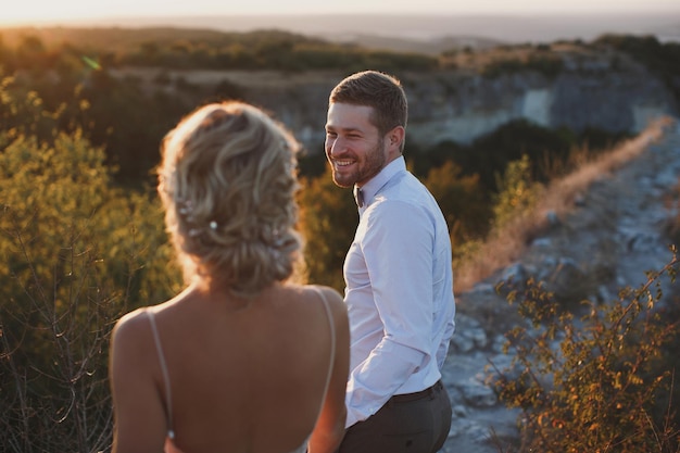 The groom is holding the bride's hand at the top of the mountain follow me