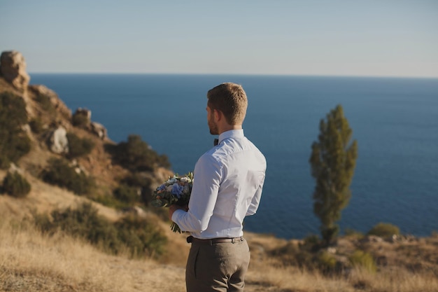 The groom is waiting for the bride on the background of the blue sea