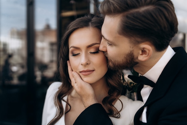 The groom kisses the beautiful bride on her cheek. portrait of a cute newly married couple close up. man kisses a woman