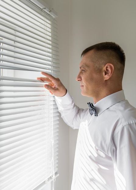 The groom looks through the blinds Waiting for the bride Anxiety before the wedding