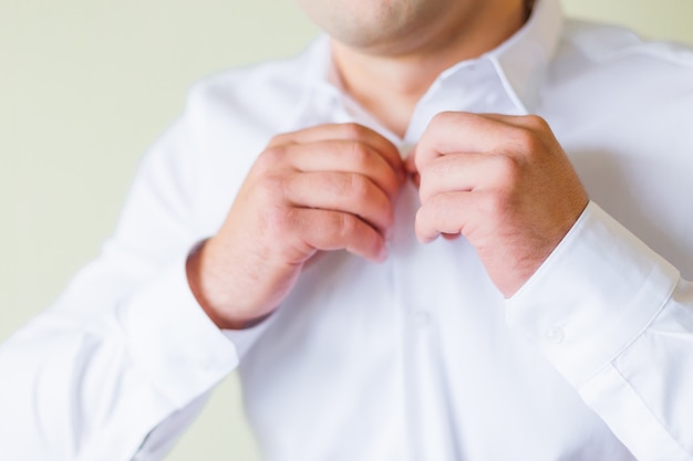 Groom pinches buttons on white shirt. close up.