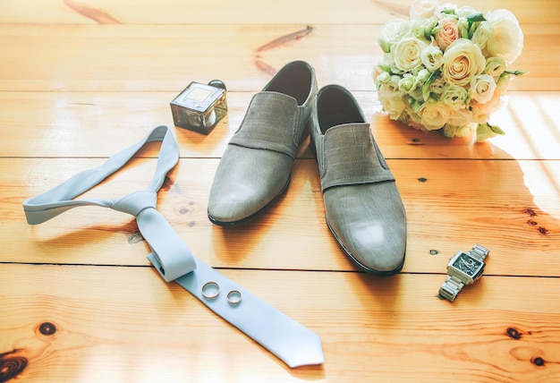 Groom's grey shoes blue tie and watch on the wooden background Wedding details photo Bouquet rings and perfumes accessories