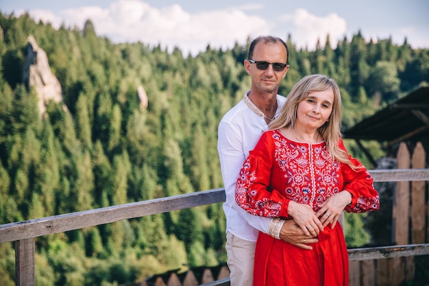 The groom's parents in each other's arms looking at the camera against the backdrop of the forest. mom and dad in embroidered clothes.