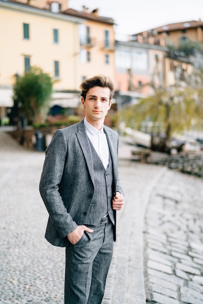 Groom stands on the cobblestones of the street in varenna