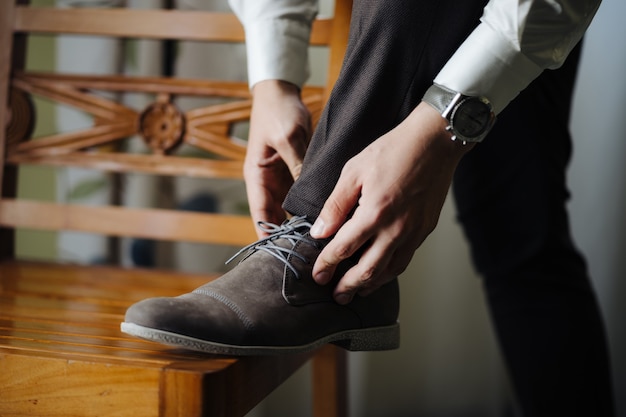 Groom straightens the laced laces with his foot on the chair