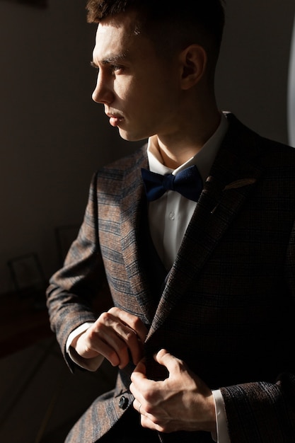 A groom in a suit in the harsh sunlight buttons up his suit