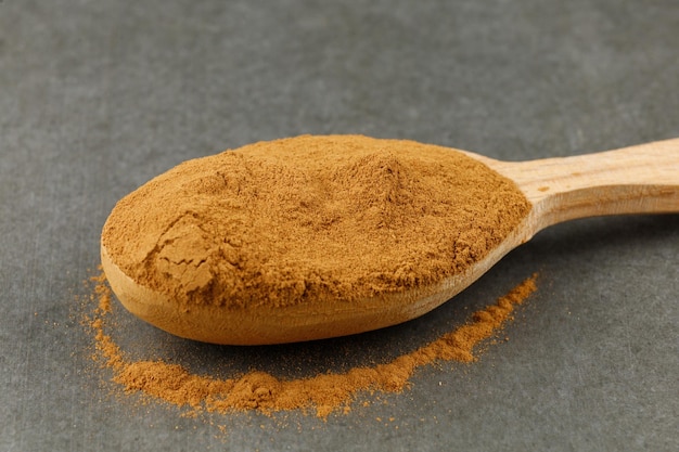 Ground cinnamon in a spoon on a gray background