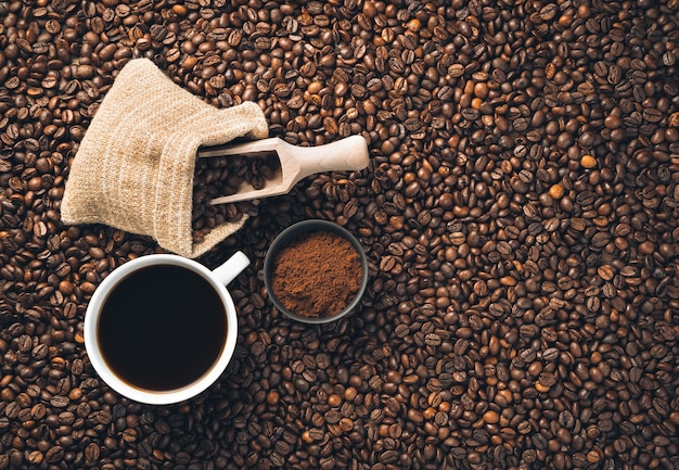 Ground coffee, coffee beans and a cup of coffee on scattered coffee beans. Top view, horizontal.