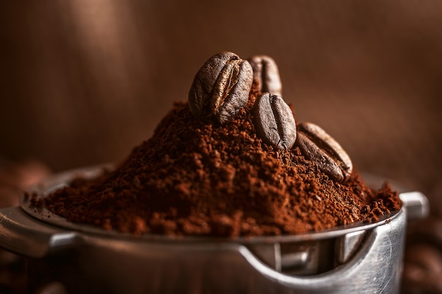 Ground coffee poured into the holder on which the grains of roasted, fragrant coffee lie. on the background of fried grains