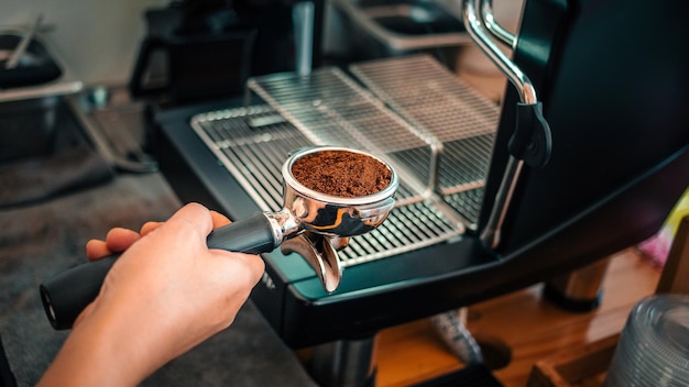 Ground coffee powder in filter and coffee tamper making an espresso coffee in the barista's hand