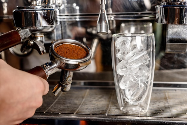 Ground coffee with a glass of ice cubes a barista prepares a coffee drink