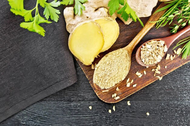 ground ginger and flakes in two wooden spoons, ginger root, spicy herbs, napkin on board 