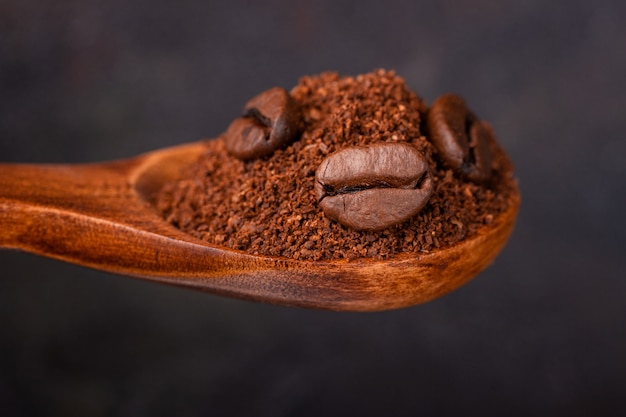 Ground and grain coffee in a wooden spoon against a dark background