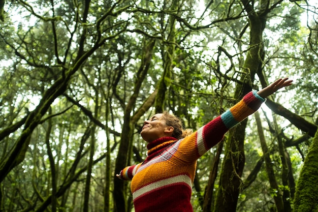 Ground view of joyful woman with arms up standing in the deep forest Nature environment activist people Love for forest and natural places Save Our planet earth High top trees in background