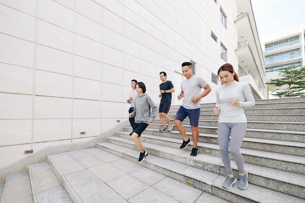 Group of active young Asian people jogging down the stairs outdoors in the morning