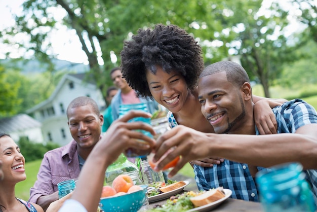 A group of adults and young people at a meal in the garden of a farmhouse Passing plates and raising