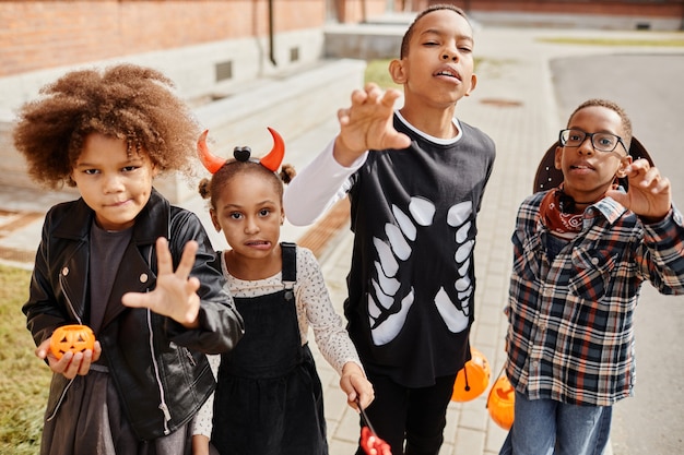 Group of africanamerican kids wearing halloween costumes and posing for camera while trick or treati...