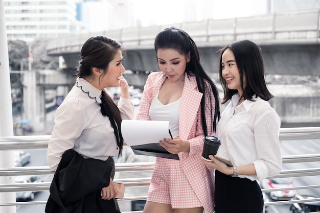 Group of Asian business woman are looking at information in the workbook with smile at outdoor in city. Concept of teamwork asian woman. Thai women office worker group.