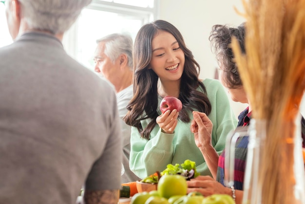 Group of asian elder senior friends at dinner party at home senior friend preparing salad and fruit juice with her daughter with smiling cheerful moment conversation with elder friend laugh smile