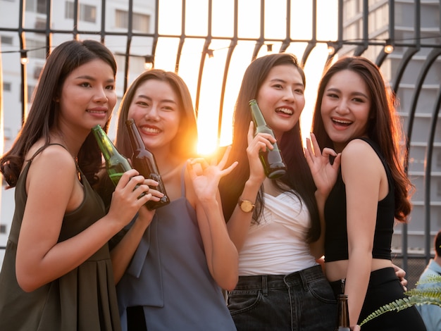 Group of asian friend cheering and drinking at terrace party. Young people enjoying and hanging out on rooftop at sunset