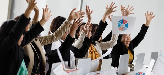 Group of Asian middle aged female happy successful businesswoman in formal suit sitting raised hands up hooray throwing document paperwork when achieve company business target goal together in office.