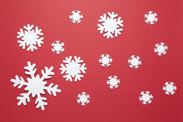 Group of big and small white felt snowflakes on burgundy red. 