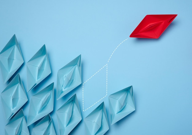 A group of blue paper boats and one red one moving in the opposite direction the concept of independent personality and breaking away from influence