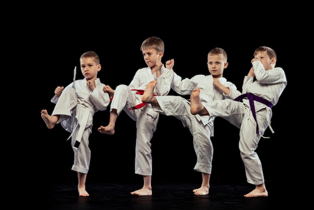 Group of boys children training martial arts karate isolated over black studio background Sportive lifestyle