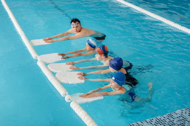 A group of boys and girls train and learn to swim in the pool with an instructor. Development of children's sports.