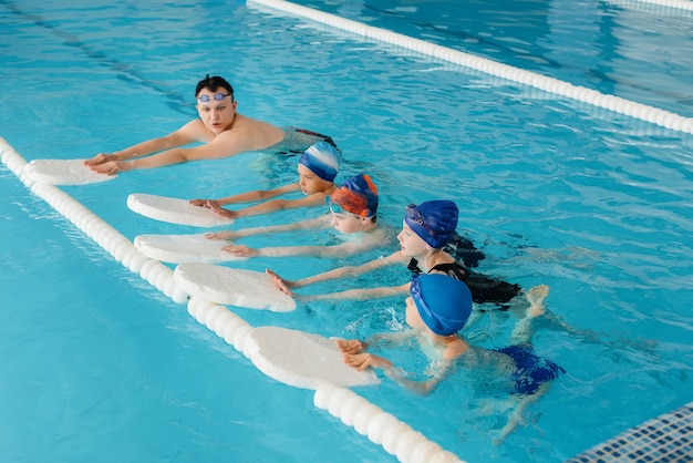 A group of boys and girls train and learn to swim in the pool with an instructor. Development of children's sports.