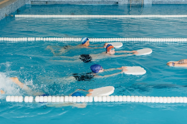 A group of boys and girls train and learn to swim in the pool with an instructor. Development of children's sports.