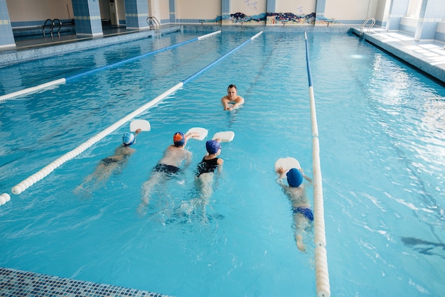 A group of boys and girls train and learn to swim in the pool with an instructor. Development of children's sports.