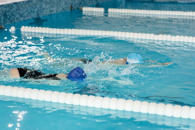 A group of boys and girls train and learn to swim in the pool with an instructor. Development of children's sports.